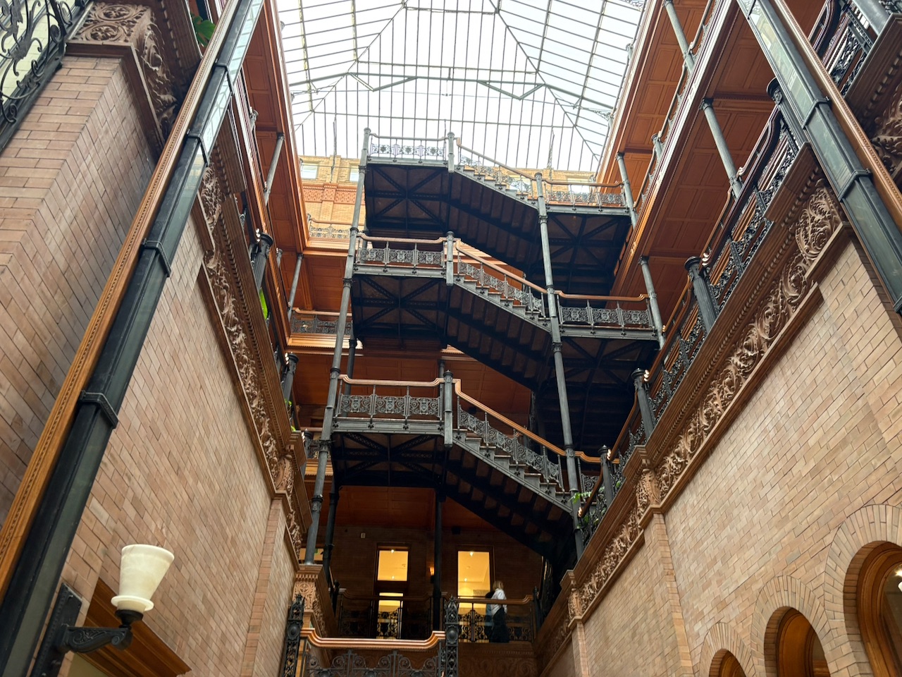 The Bradbury Building atrium looking up - cast-iron railings, open-cage elevators, and a glass roof flooding the space with light