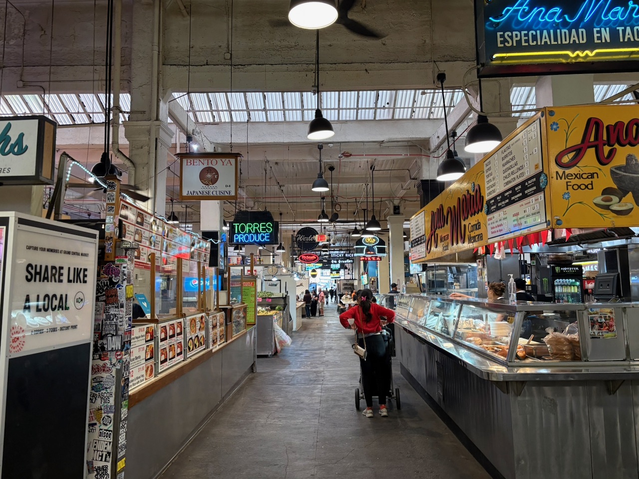 The bustling interior of Grand Central Market with its food vendors, neon signs, and shoppers
